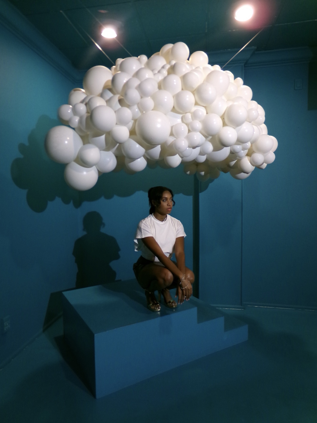Iyana Admasu posing beneath a suspended balloon-cloud art installation