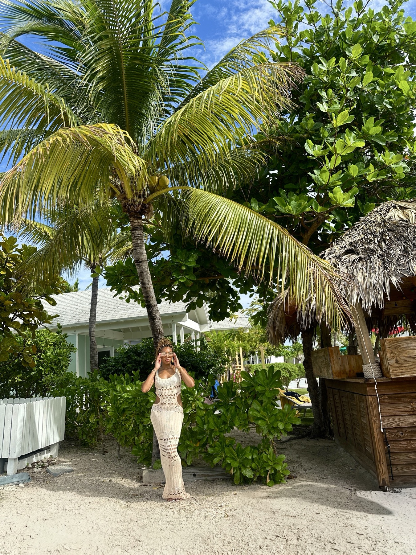 Iyana Admasu posing beneath a palm tree in a crochet dress on a beach