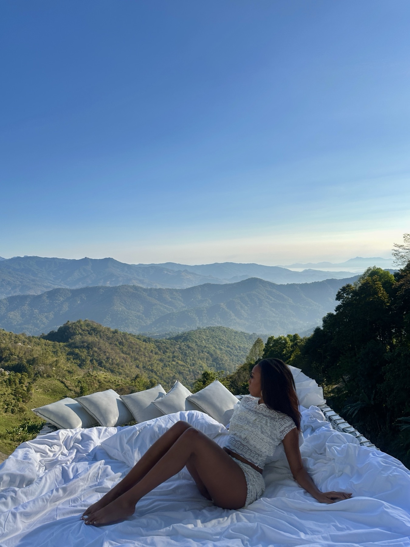 Editorial travel portrait overlooking misty mountains from a hillside daybed