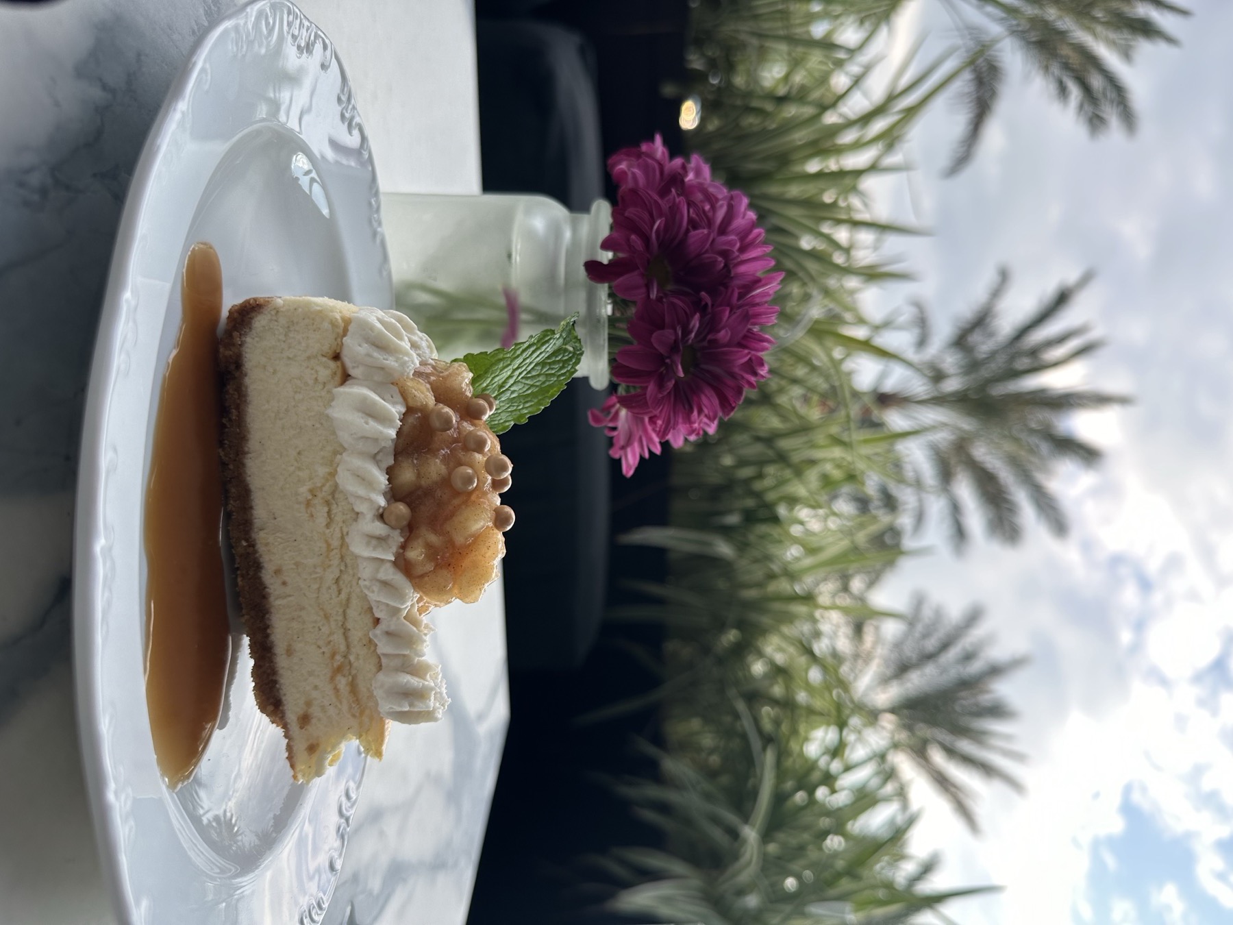 Cheesecake slice plated with caramel, mint, and fresh flowers